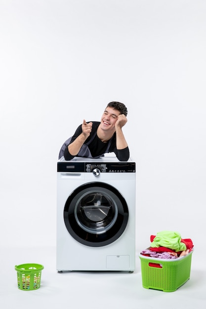 白い壁に洗濯機と汚れた服を着た若い男性の正面図