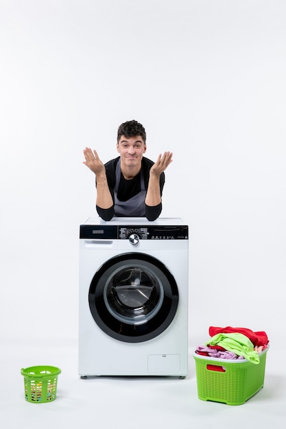 Front view of young male with washer and dirty clothes on white wall