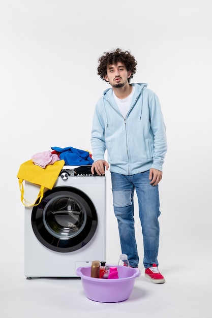 Вид спереди молодого мужчины с стиральной машиной и грязной одеждой на белой стене