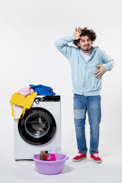 Front view of young male with washer and dirty clothes on white wall