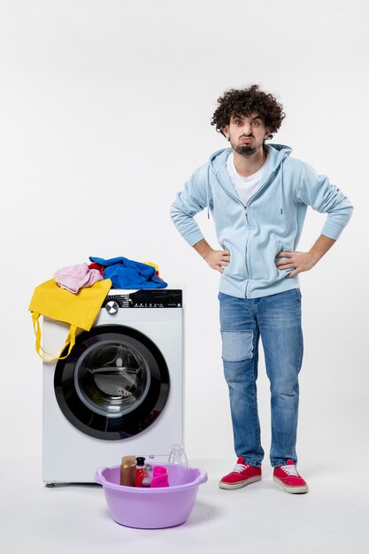 Front view of young male with washer and dirty clothes on white wall