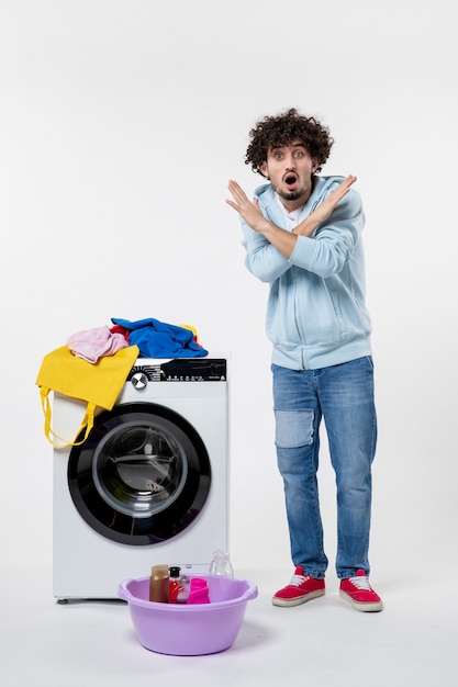 白い壁に洗濯機と汚れた服を着た若い男性の正面図