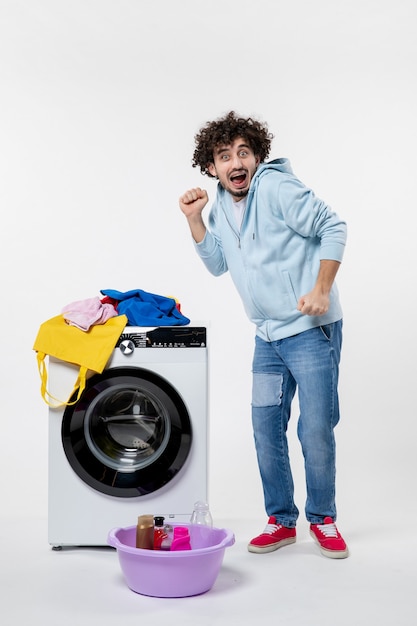 Foto gratuita vista frontale del giovane maschio con lavatrice e vestiti sporchi sul muro bianco