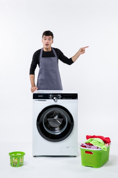 Front view of young male with washer and dirty clothes on white wall