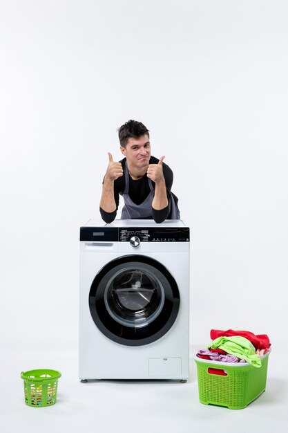 Front view of young male with washer and dirty clothes on white wall