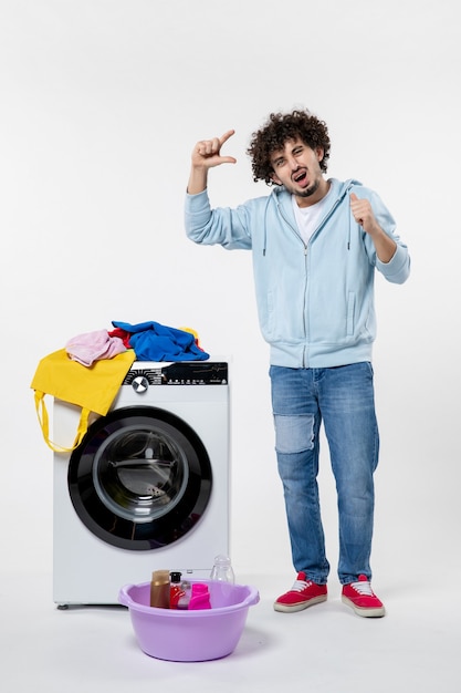 Front view of young male with washer and dirty clothes on white wall