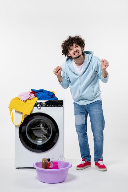 Вид спереди молодого мужчины с стиральной машиной и грязной одеждой на белой стене