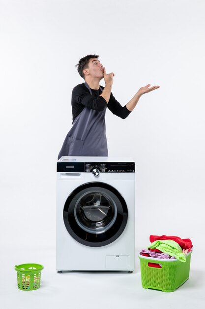 Front view of young male with washer and dirty clothes on white wall