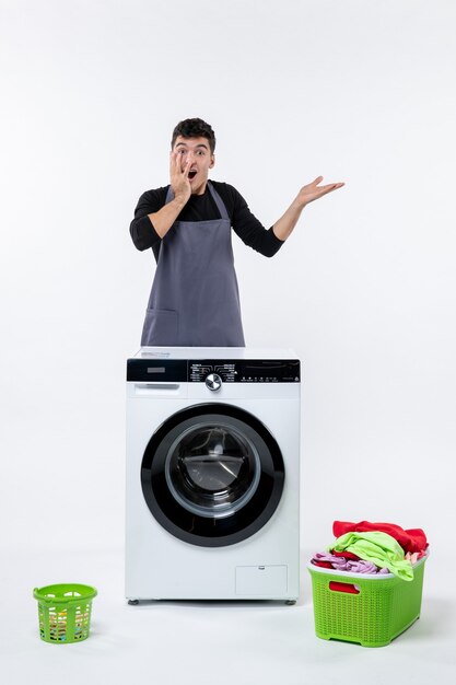 Front view of young male with washer and dirty clothes on white wall