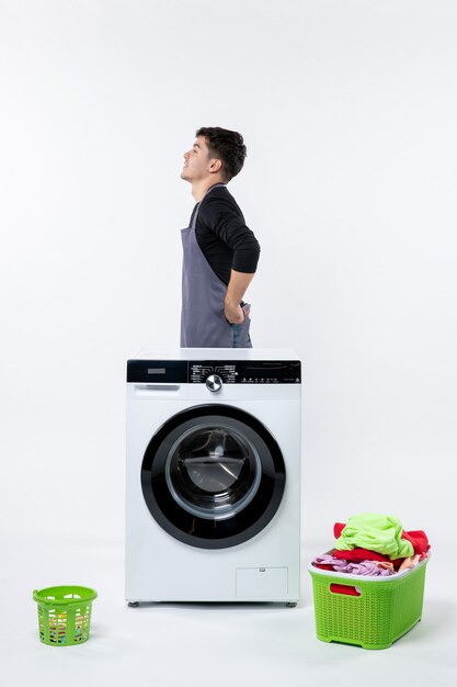 Front view of young male with washer and dirty clothes on white wall