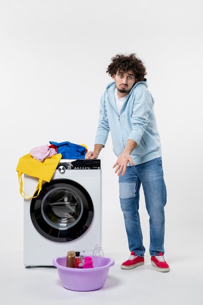 Front view of young male with washer and dirty clothes on white wall