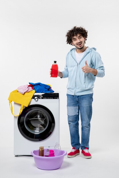 Front view of young male with washer and dirty clothes on white wall