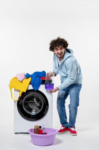 Front view of young male with washer holding liquid powder on the white wall