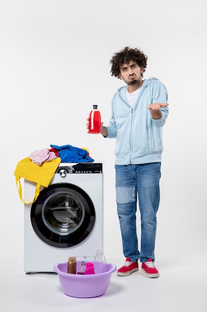 白い壁に液体粉末を保持している洗濯機を持つ若い男性の正面図