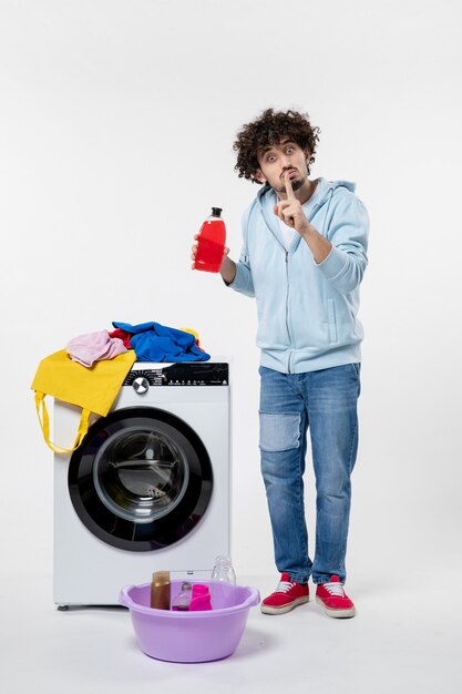 Front view of young male with washer holding liquid powder on the white wall