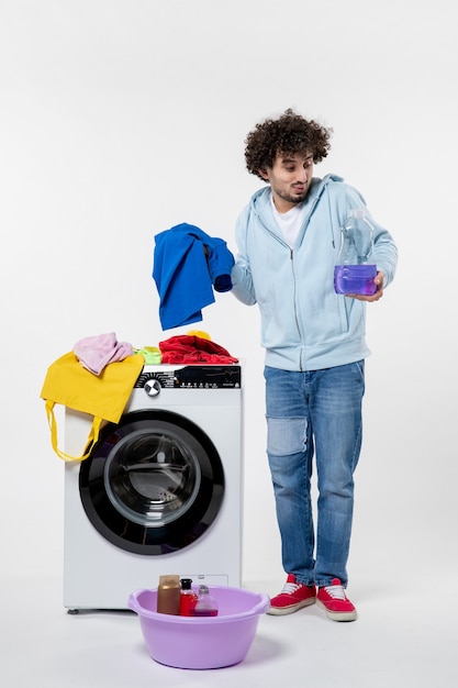 Front view of young male with washer holding liquid powder on white wall