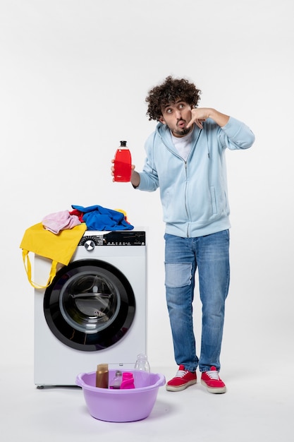 Front view of young male with washer holding liquid powder on white wall