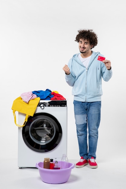 Front view of young male with washer holding red bank card rejoicing on white wall