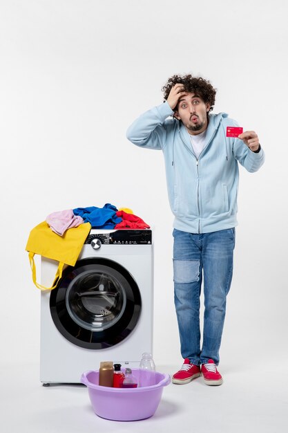 Front view of young male with washer holding red bank card on a white wall