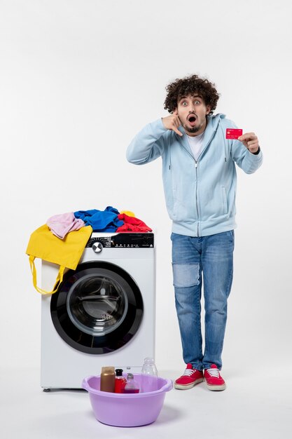 Front view of young male with washer holding red bank card on white wall