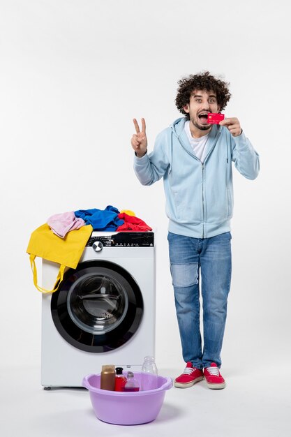 Front view of young male with washer holding red bank card on white wall