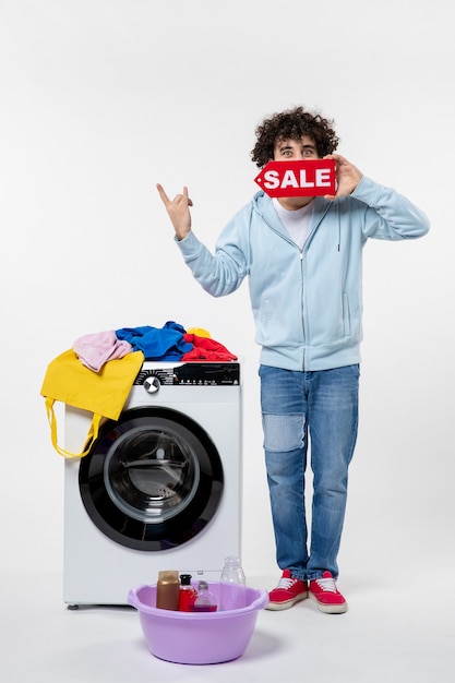 白い壁に赤い販売バナーを保持している洗濯機を持つ若い男性の正面図