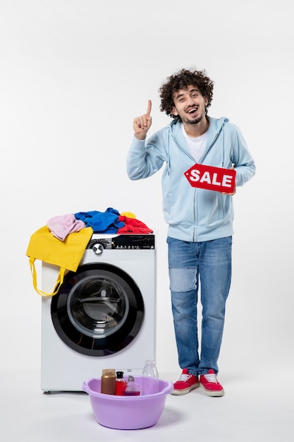 Front view of young male with washer holding red sale banner on the white wall