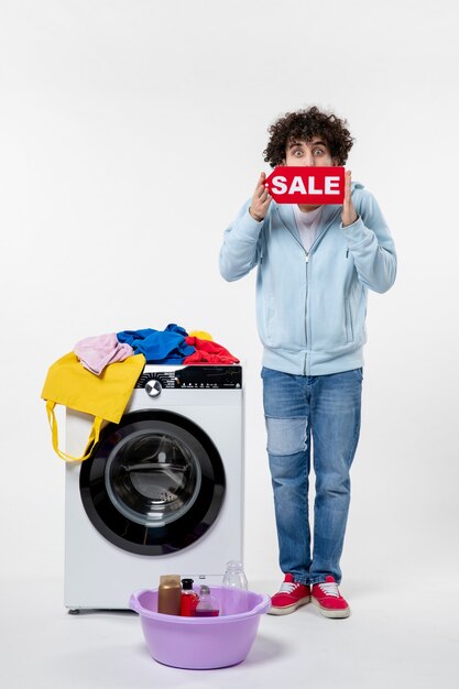 白い壁に赤い販売バナーを保持している洗濯機を持つ若い男性の正面図
