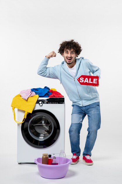 Front view of young male with washer holding red sale banner on white wall