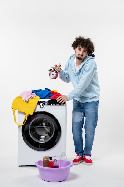 Front view of young male with washer waiting until the end of clothes washing on white wall
