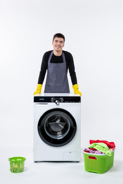 Вид спереди молодого мужчины со стиральной машиной и грязной одеждой на белой стене
