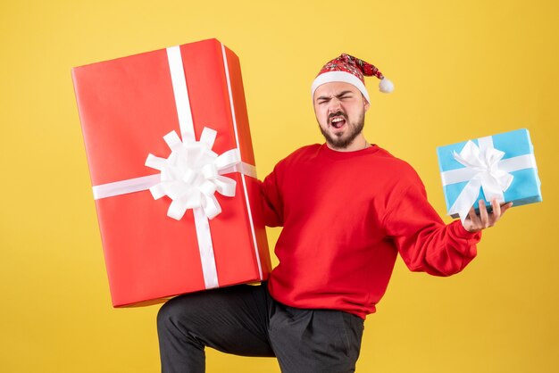 Вид спереди молодой мужчина с рождественскими подарками на желтом фоне