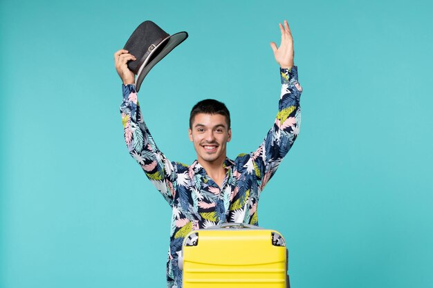 Front view of young male with yellow bag holding hat and preparing for trip on light blue wall