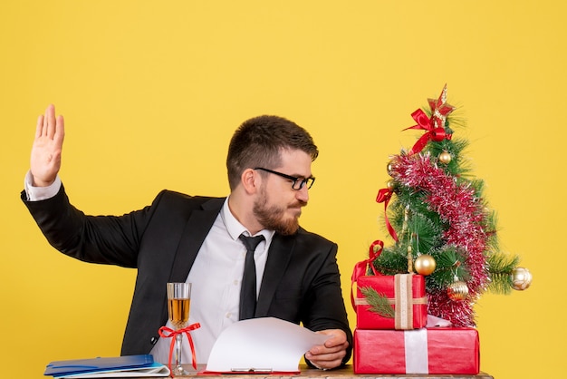 Front view young male worker behind his table with presents and xmas tree on yellow 