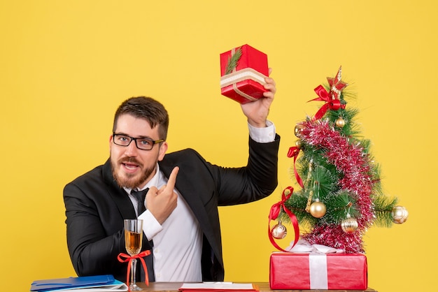 黄色のプレゼントとクリスマスツリーと彼のテーブルの後ろの正面図若い男性労働者