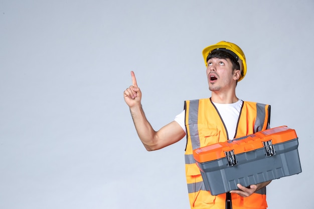 Front view young male worker holding heavy tool case on white background