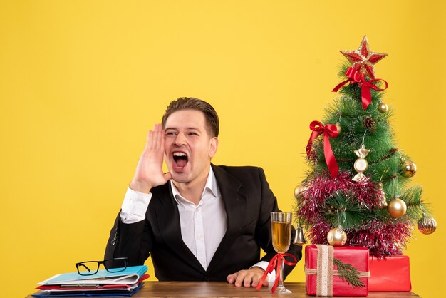 Front view young male worker sitting with xmas presents and tree calling