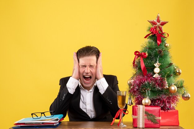 Вид спереди молодой работник-мужчина сидит с рождественскими подарками и кричит деревом
