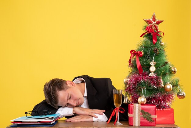 Вид спереди молодой работник-мужчина сидит с рождественскими подарками и спит на дереве