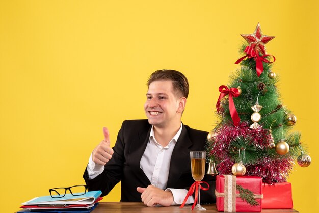 Вид спереди молодой работник-мужчина сидит с рождественскими подарками и деревом