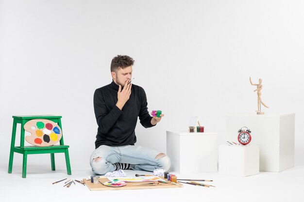 Вид спереди молодой мужчина, работающий с красками на белой стене, художник рисует искусство цветные картины картина рисует фото
