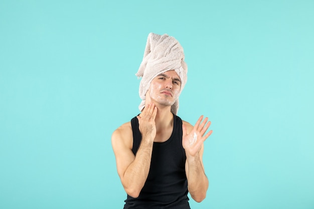 Free photo front view of young man after shower applying cream to his face on blue wall