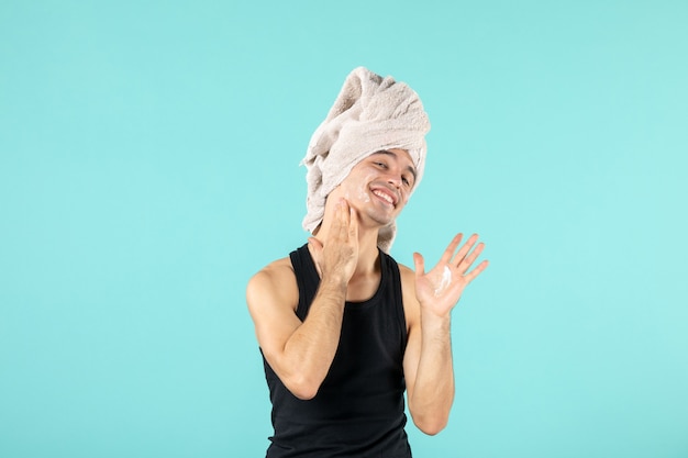 Free photo front view of young man after shower applying cream to his face on blue wall