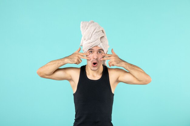 front view of young man after shower applying cream to his face on blue wall