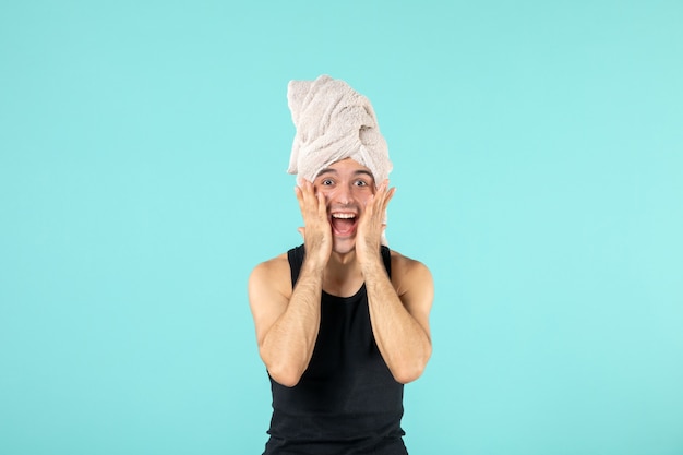 front view of young man after shower applying cream to his face on blue wall