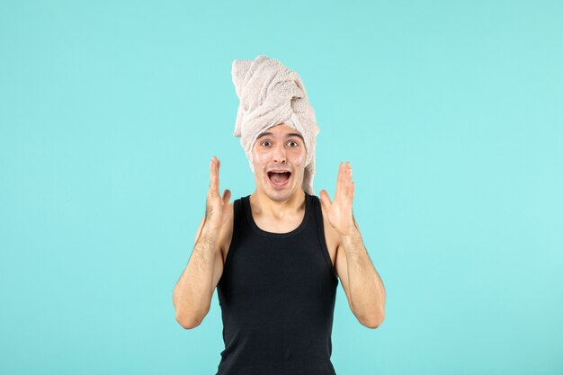 front view of young man after shower applying cream to his face on blue wall