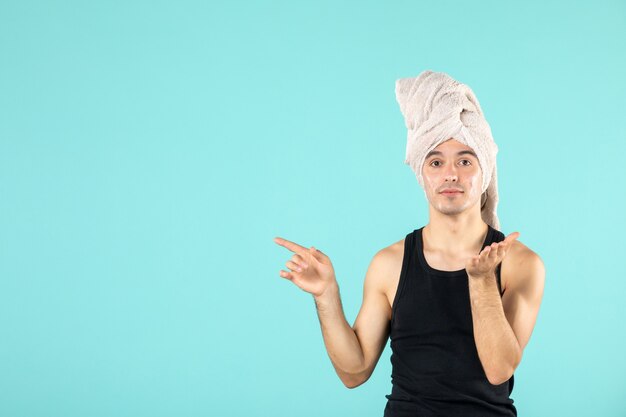 front view of young man after shower applying cream to his face on blue wall