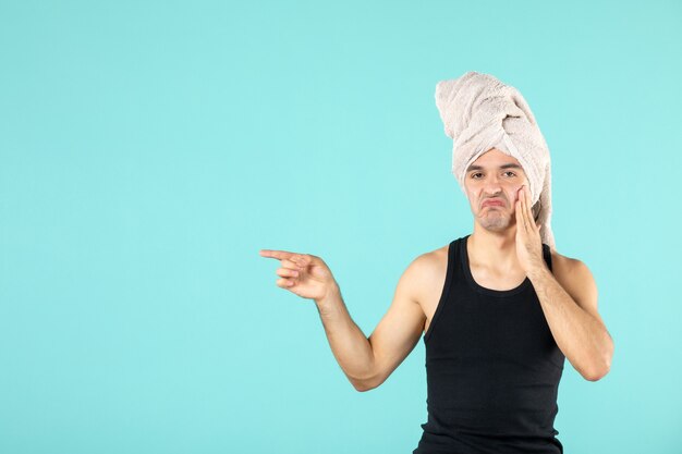 front view of young man after shower applying cream to his face on blue wall