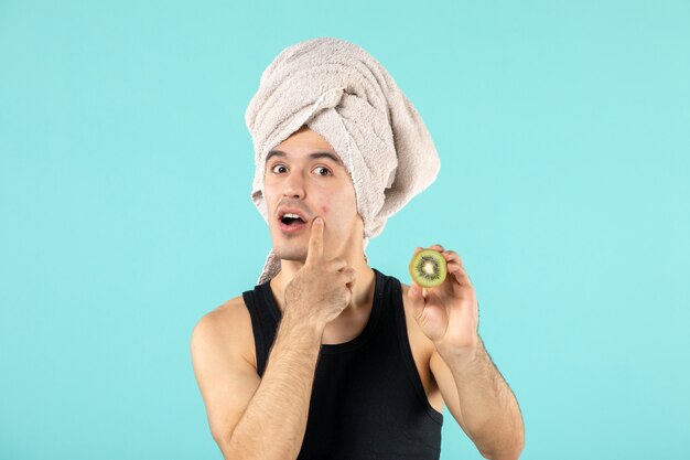 front view of young man after shower holding kiwi slices on blue wall