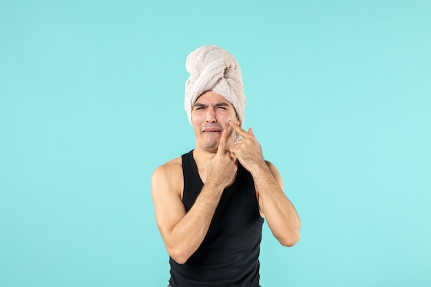 front view of young man after shower trying to squeeze out little pimple on blue wall